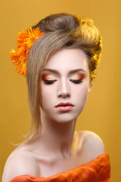 Fashion beauty portrait of girl with orange makeup on yellow background.