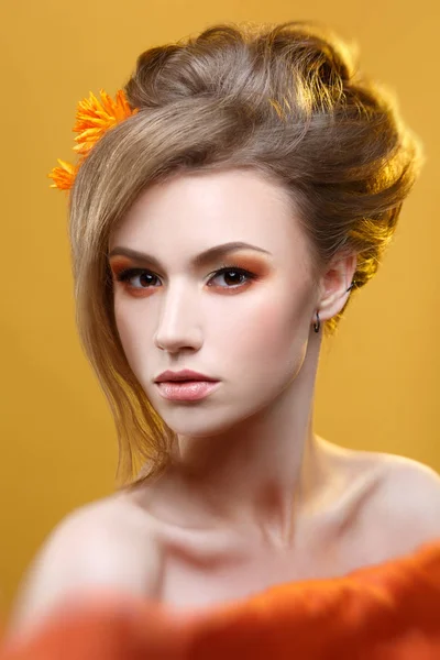 Fashion beauty portrait of girl with orange makeup on yellow background.