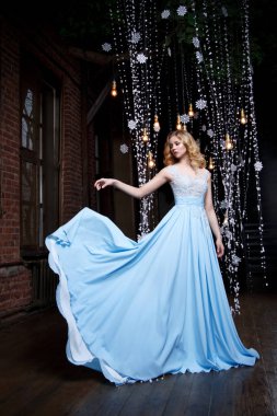 Karanlık bir arka plan üzerinde uzun mavi elbiseli güzel sarışın kız.