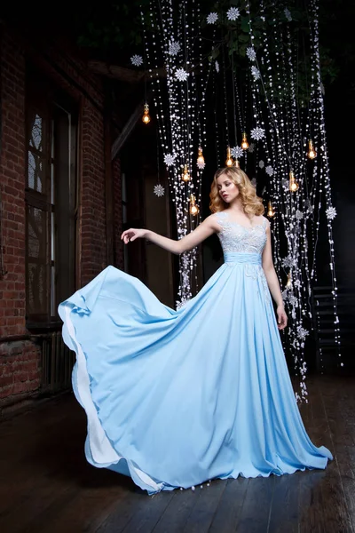 Karanlık bir arka plan üzerinde uzun mavi elbiseli güzel sarışın kız.