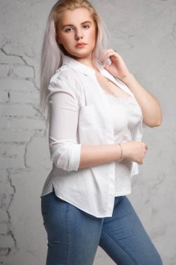 Oldukça büyük bir sarışın gri bir arka plan üzerinde beyaz gömlekli portresi.