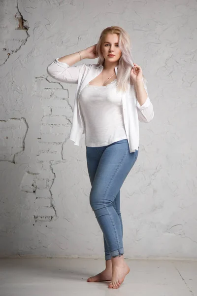 Oldukça büyük bir sarışın gri bir arka plan üzerinde beyaz gömlekli portresi.