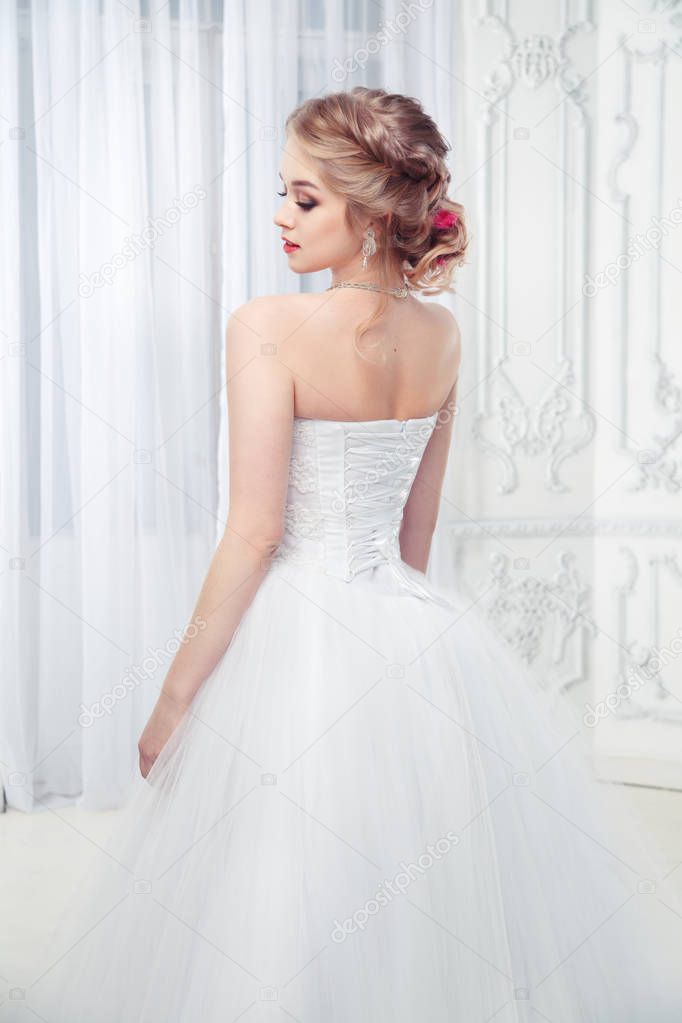 Lovely bride blonde with a beautiful hairdo in a dress with lacing look from the back.