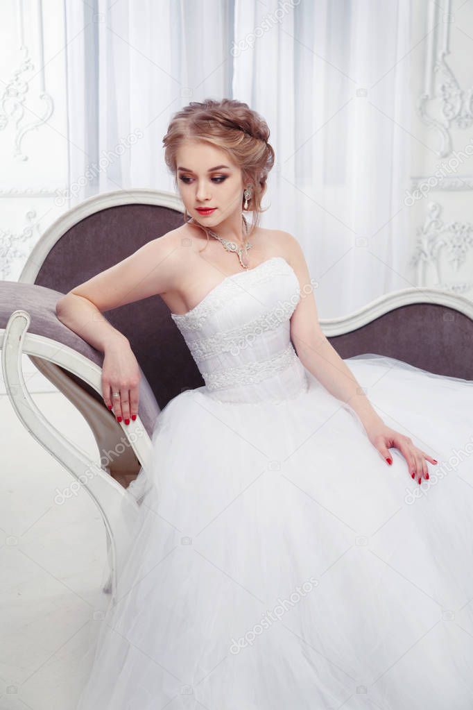 A sweet bride in a beautiful dress sitting  in an armchair in a chic, light interior.