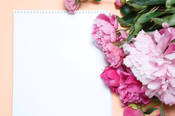 A bouquet of pink peonies and a sheet of white paper rests on a background of salmon-colored .