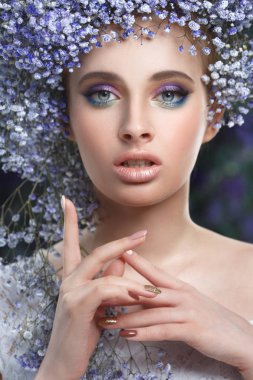 Küçük mavi çiçeklerden yapılmış bir hacimli çelenk içinde güzel bir kız moda güzellik portresi.