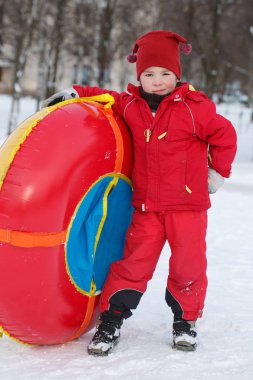 Kırmızı tulum bir çocuk ile bir boru bir kış parkta duruyor.
