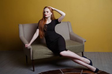 Kızıl saçlı Genç kız kanepe üzerinde poz siyah gece elbisesi içinde