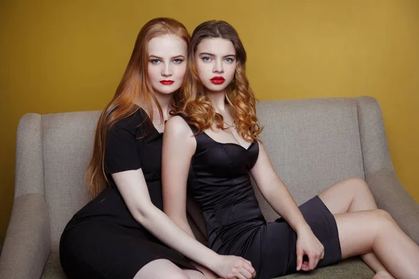 年轻的红头发妇女坐在沙发上与黄色的墙壁背景 — 图库照片