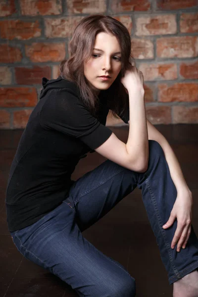 young pensive woman in casual clothes posing on brick wall background