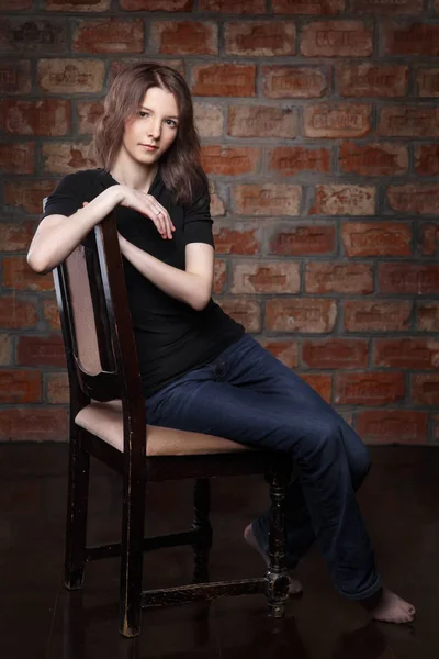 young woman in casual clothes sitting on chair on brick wall background
