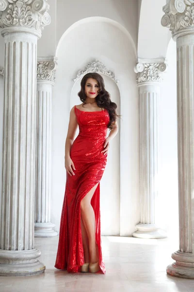 attractive woman in red shiny dress standing in room with white columns