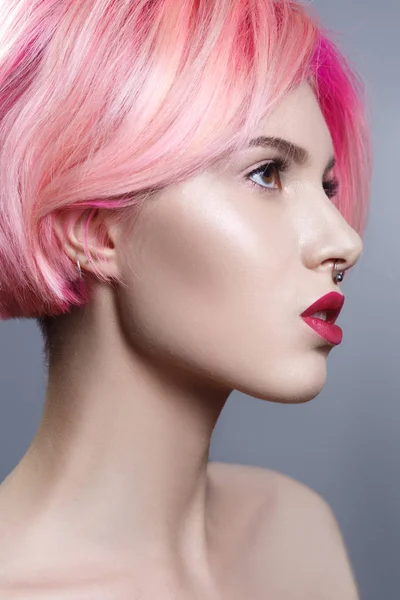 Portrait of young woman with pink hair on gray background