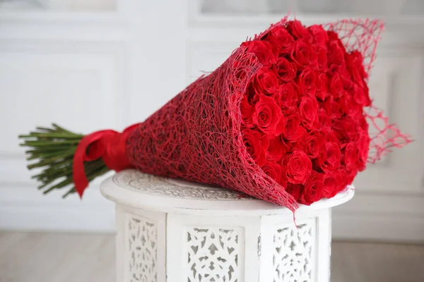 在明亮的内部雕刻的床头柜上的一大束红玫瑰 — 图库照片