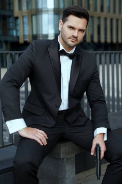 Elinde silah olan zarif adam şehrin arka planında oturuyor..