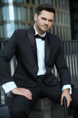 Elinde silah olan zarif adam şehrin arka planında oturuyor..