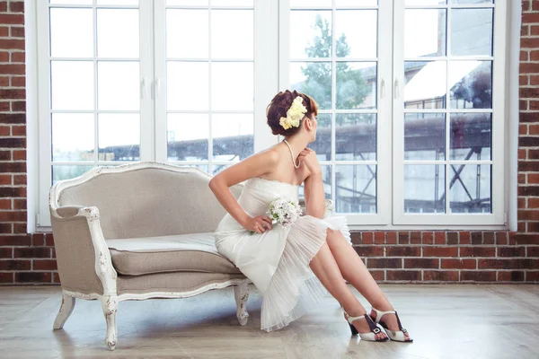 Elegant Bride sitting on the couch and looked at the large window in a stylish loft