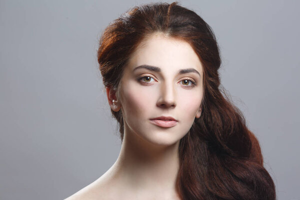 Beauty portrait of a cute girl with long chic hair isolated on a gray background.