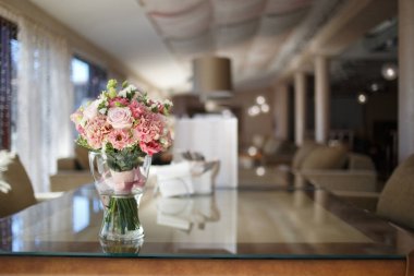 Delicate wedding bouquet in pink tones of roses and lisianthus is in a glass vase on the table in the restaurant.