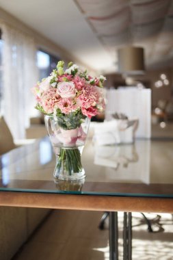 Delicate wedding bouquet in pink tones of roses and lisianthus is in a glass vase on the table in the restaurant.