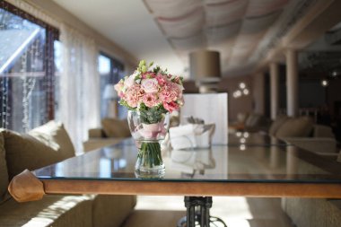 Delicate wedding bouquet in pink tones of roses and lisianthus is in a glass vase on the table in the restaurant.