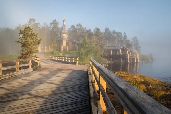Landscape with a church and a bridge on a lake in the rays of a low sun in the fog, Valaam Island, Karelia, Russia.