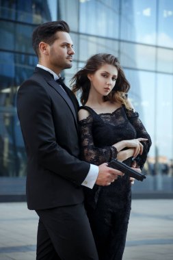An elegant man with pistols in his hands protects a beautiful girl. clipart