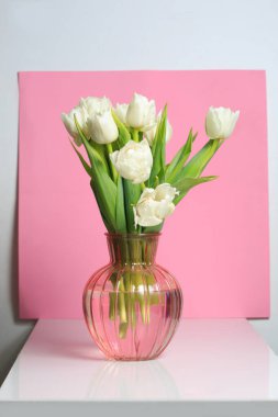 Sahne arkasında pembe arka planda cam vazoda beyaz laleler..