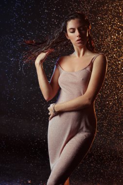 Yüzüne damla damla su damlatan güzel seksi bir kız. Stüdyonun arka planında turuncu bir ışıkla aydınlatılmış..