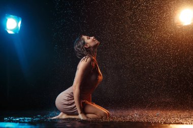 Yüzüne damla damla su damlatan güzel seksi bir kız. Stüdyonun arka planında turuncu bir ışıkla aydınlatılmış..
