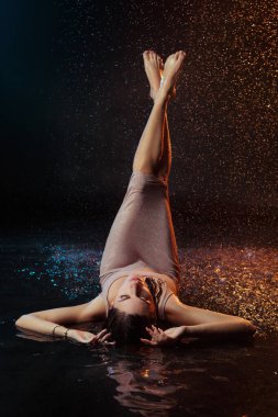 Yüzüne damla damla su damlatan güzel seksi bir kız. Stüdyonun arka planında turuncu bir ışıkla aydınlatılmış..