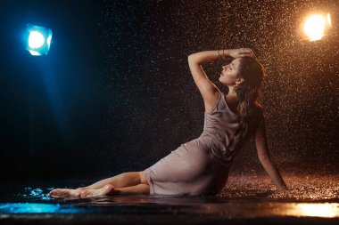 Yüzüne damla damla su damlatan güzel seksi bir kız. Stüdyonun arka planında turuncu bir ışıkla aydınlatılmış..