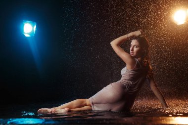 Yüzüne damla damla su damlatan güzel seksi bir kız. Stüdyonun arka planında turuncu bir ışıkla aydınlatılmış..