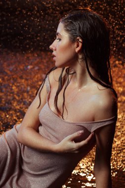 Yüzüne damla damla su damlatan güzel seksi bir kız. Stüdyonun arka planında turuncu bir ışıkla aydınlatılmış..