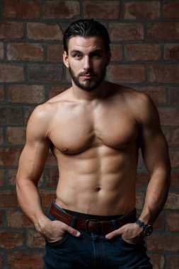 Tuğla bir duvarın arkasında çıplak bir gövdesi olan genç ve çekici bir atletik..