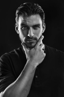 Siyah-beyaz bir portre. Siyah bir arka planda, yüzünün yakınında elini tutan cesur ve çekici bir adam..