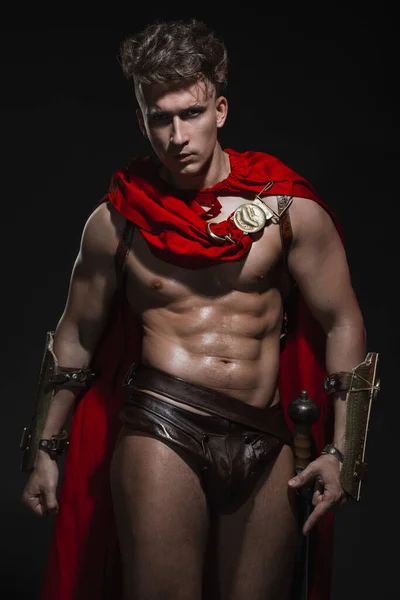 Siyah arka planda kırmızı pelerinli Romalı savaşçı kostümlü genç atletik seksi adam..