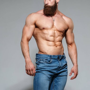 Atletik yakışıklı sakallı, kaslı, çıplak, mavi kot pantolonlu, gri arka planda yalnız bir adam..