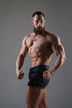 Bazı şortlu atletik kaslı adam gri arka planda izole olmuş kasları gösteriyor..