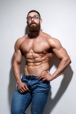 Açık gri bir arka planda çıplak kabartmalı gövdesi olan atletik sakallı adam..