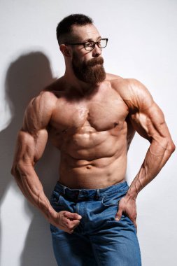 Açık gri bir arka planda çıplak kabartmalı gövdesi olan atletik sakallı adam..