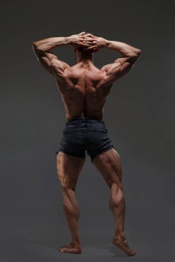 Çıplak gövdeli atletik bir adamın portresi koyu gri bir arka planda izole edilmiş kasları gösteriyor, arkadan tam boy..