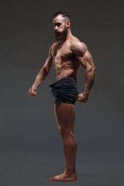 Çıplak gövdeli atletik bir adamın portresi koyu gri bir arka planda izole edilmiş kasları gösteriyor..