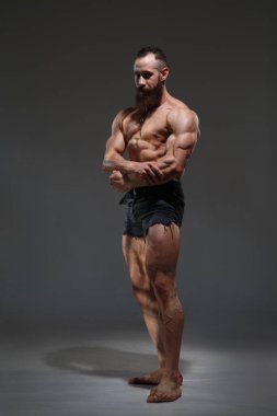 Çıplak gövdeli atletik bir adamın portresi koyu gri bir arka planda izole edilmiş kasları gösteriyor..