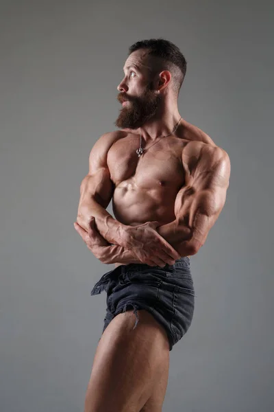 いくつかのショートパンツの運動筋の男性は灰色の背景に隔離された筋肉を示しています — ストック写真