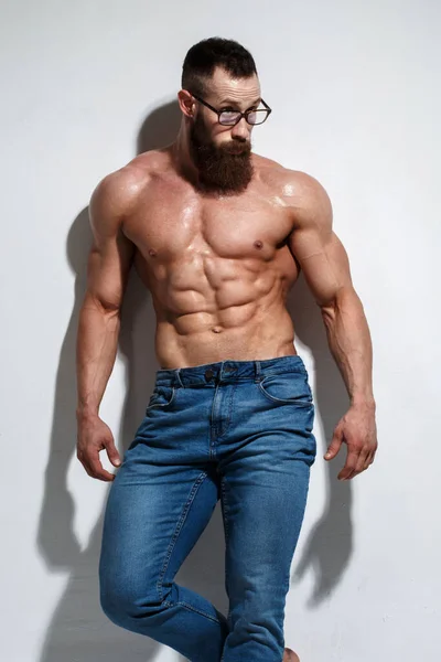 Açık gri bir arka planda çıplak kabartmalı gövdesi olan atletik sakallı adam..