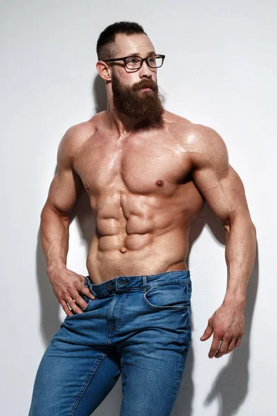 Açık gri bir arka planda çıplak kabartmalı gövdesi olan atletik sakallı adam..