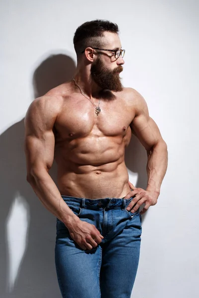 Açık gri bir arka planda çıplak kabartmalı gövdesi olan atletik sakallı adam..