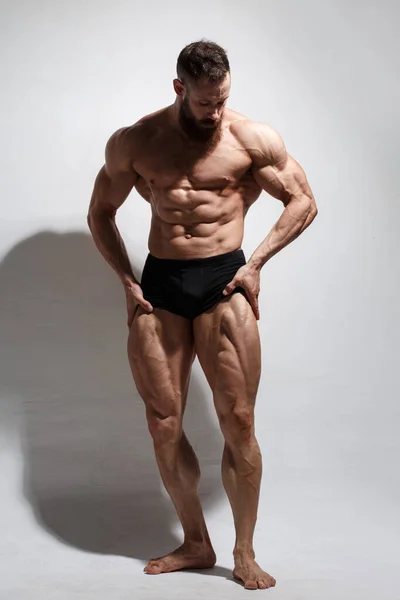 一个体格健壮 留着胡子的男人在轻盈的背景下表现出完全生长的肌肉 — 图库照片