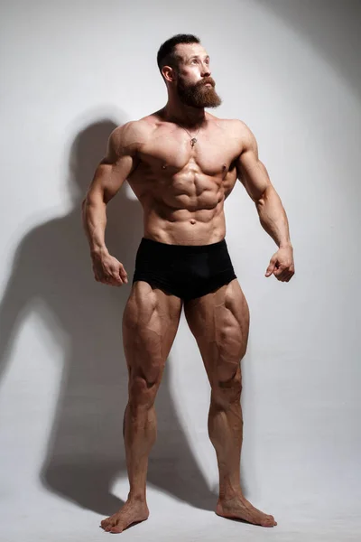 一个体格健壮 留着胡子的男人在轻盈的背景下表现出完全生长的肌肉 — 图库照片